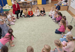 Dzieci (zgromadzone w kole na dywanie) podczas zajęć z pedagogiem i psychologiem.