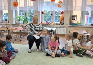 Dzieci (zgromadzone w kole na dywanie) podczas zajęć z pedagogiem i psychologiem.