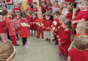 Dzieci (wszystkie w czerwinych strojach) tworzą długi łańcuch z czerwonych, papierowych serduszek.