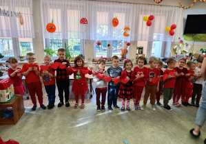 Dzieci (wszystkie w czerwinych strojach) tworzą długi łańcuch z czerwonych, papierowych serduszek.