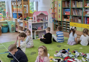 Dzieci siedzą na dywanie tyłem do skarpetek rozłożonych w środku koła.