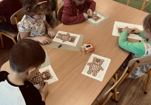 Dzieci wyklejają kuleczki z plasteliny, którymi wypełniają białe punkty w postaci misia.