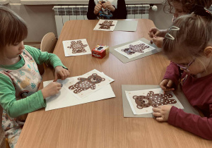 Dzieci wyklejają kuleczki z plasteliny, którymi wypełniają białe punkty w postaci misia.