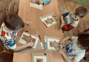 Dzieci wyklejają kuleczki z plasteliny, którymi wypełniają białe punkty w postaci misia.