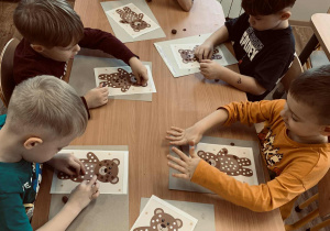 Dzieci wyklejają kuleczki z plasteliny, którymi wypełniają białe punkty w postaci misia.