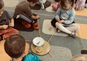 Przedszkolaki nawlekają na sznurki makaronowe rurki.