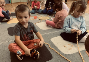 Przedszkolaki nawlekają na sznurki makaronowe rurki.