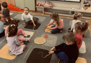 Przedszkolaki nawlekają na sznurki makaronowe rurki.