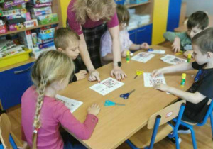 Dzieci siedzą przy stolikach. Wycinają, układają i przyklejają kolejne obrazki z polskimi symbolami uzupełniając diagram sudoku.
