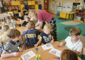 Dzieci siedzą przy stolikach. Wycinają, układają i przyklejają kolejne obrazki z polskimi symbolami uzupełniając diagram sudoku.