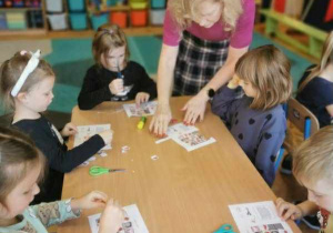 Dzieci siedzą przy stolikach. Wycinają, układają i przyklejają kolejne obrazki z polskimi symbolami uzupełniając diagram sudoku.