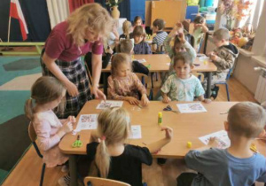 Dzieci siedzą przy stolikach. Wycinają, układają i przyklejają kolejne obrazki z polskimi symbolami uzupełniając diagram sudoku.