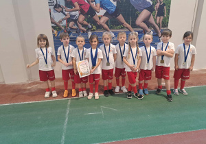 Dzieci w sportowych strojach trzymają dyplomy i prezentują medale.
