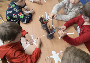 Dzieci wykonują (przy stolikach) papierowe kukiełki.