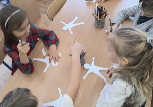 Dzieci wykonują (przy stolikach) papierowe kukiełki.