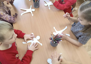 Dzieci wykonują (przy stolikach) papierowe kukiełki.