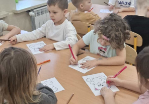 Dzieci siedzą przy stolikach i kolorują misie.