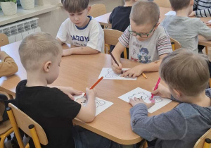 Dzieci siedzą przy stolikach i kolorują misie.