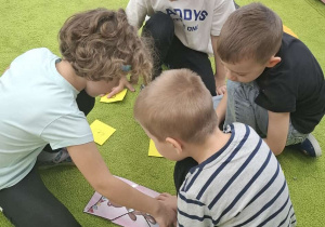 Dzieci siedzą na dywanie w kilkuosobowych grupach i układają puzzle.