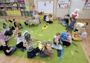 Dzieci siedzą w kręgu i trzymają swoje pluszowe zabawki.