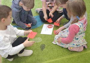 Dzieci siedzą na dywanie w kilkuosobowych grupach i układają puzzle.