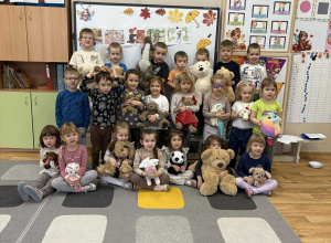 Dzieci stoją na dywanie w sali i prezentują swoje misie.