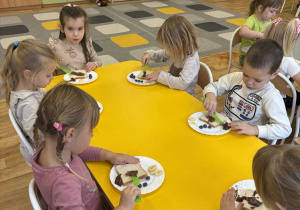 Dzieci przy stoliku komponują kanapki w kształcie misia.