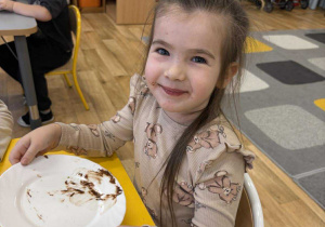 Dziewczynka zadowolona pokazuje swoją ubrudzoną od Nutelli buzię.