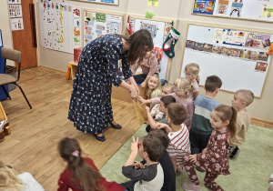 Harfistka prezentuje dzieciom instrument, a dzieci go dotykają.