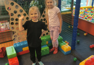 Dwie dziewczynki pozują do zdjęcia przy budowli z klocków.