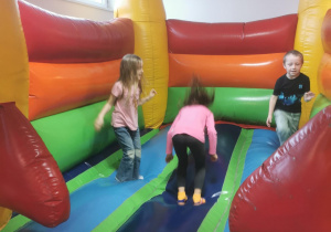 Troje dzieci skacze na dmuchanym zamku