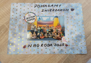 Pamiątkowe grupowe zdjęcie dzieci wraz z nauczycielkami na tle dmuchanego zamku. Zdjęcie podpisane "Pomagamy zwierzakom - nagroda".