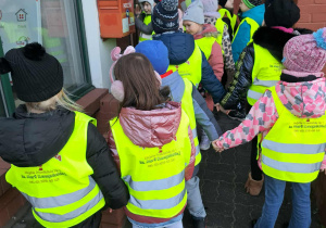 Grupa dzieci obserwuje jak ich kolega wrzuca pocztówkę świąteczną do skrzynki pocztowej.