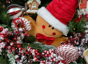 Maskotka piernikowego ludzika w otoczeniu świątecznych ozdób.