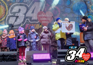 Przedszkolaki na wielkiej scenie WOŚP, prowadząca licytację trzyma obraz przygotowany na aukcję.