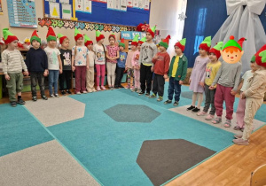 Grupa dzieci w czapeczkach elfów występuje przed emerytowanymi nauczycielkami i pracownikami przedszkkola.