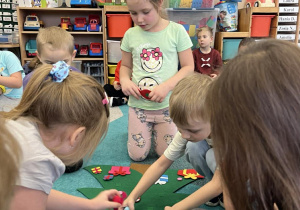 Dzieci dokładają świąteczne ozdoby według wskazówek logopedy.