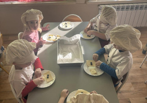 Dzieci siedzą przy stoliku i lepią ciasteczka.