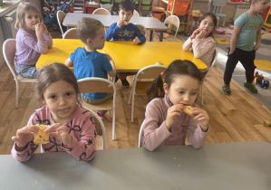 Dzieci przy stole jedzą swoje smaczne ciasteczka.