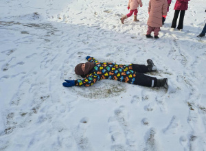 Dwoje dzieci leży na śniegu i robi tzw. „aniołka”.