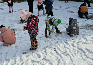 Grupa dzieci lepi kulki ze śniegu.