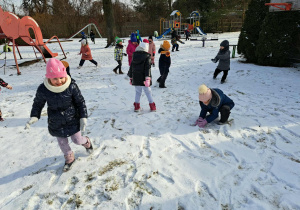 Grupa dzieci lepi kulki ze śniegu.