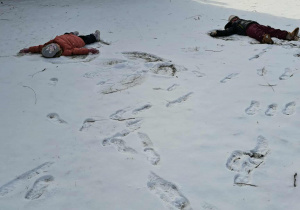 Dwoje dzieci leży na śniegu i robi tzw. „aniołka”.