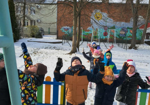 Grupa dzieci idzie gęsiego po śniegu i spogląda na niebo.