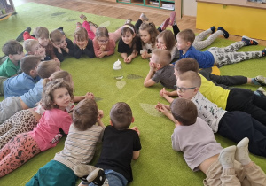 Dzieci leżą na dywanie w kole, oczekując na wykonanie eksperymentu.
