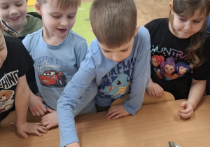 Dzieci stoją przy stoliku, chłopiec przykłada magnes do różowego piórka.