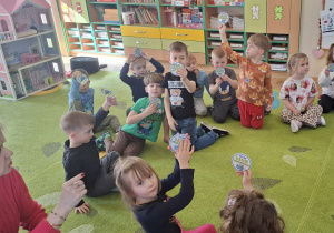 Dzieci siedzą w kręgu na dywanie i pokazują odznaki