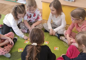 Dzieci siedzą na dywanie i grają w memory obrazkowe.