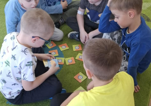 Dzieci siedzą na dywanie i grają w memory obrazkowe.