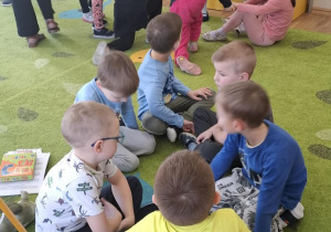 Dzieci siedzą w małych grupkach na dywanie.